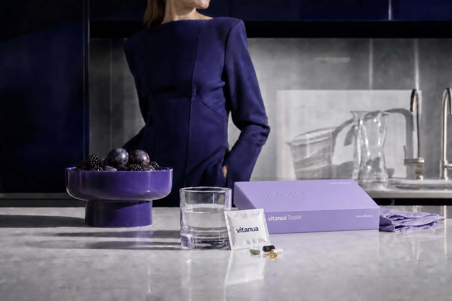 Das einheitlich gestaltete violette vitanua Testkit und ein vorportioniertes Nährstoff-Kit in einer farblich abgestimmten Navy-Küche